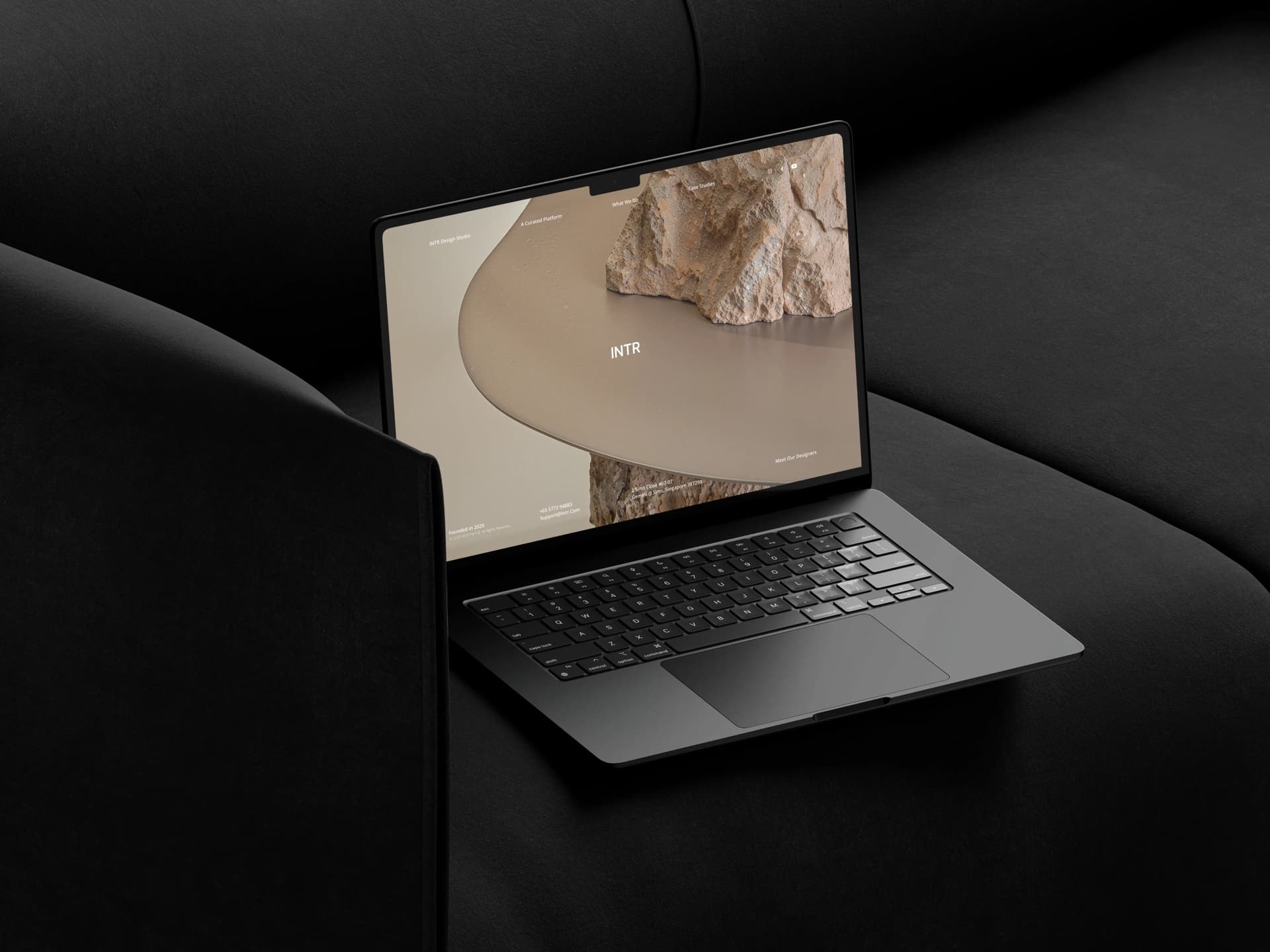 INTR website hero shown on a dark laptop resting on a charcoal sofa